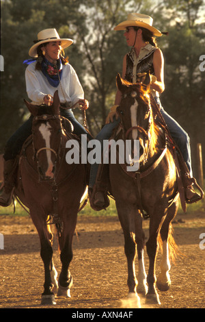 Two women dressed in cowboy clothes and hats riding horses western style on horseback at a ranch near Santa Fe New Mexico. Stock Photo