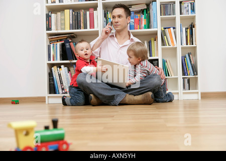 Father with two sons trying to using a mobile phone and a laptop Stock Photo