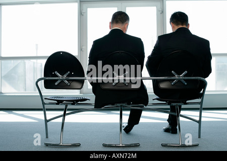 Two businessmen sitting on a bench looking down, rear view Stock Photo