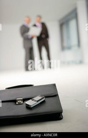 Briefcase and cell phone lying on the floor, two people in the background Stock Photo