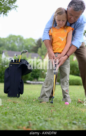 Senior adult man is teaching a girl how to play golf, selective focus Stock Photo