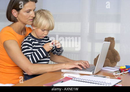 Mother using a laptop while son (4-5 Years) sitting on her lap Stock Photo