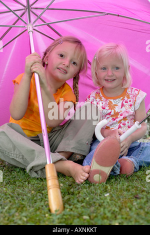 Two little girls sitting under a pink umbrella Stock Photo
