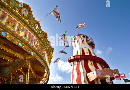 Helter-skelter at fairground with carousel merry-go-round in colourful colorful stripes and gold with flags under blue sky child Stock Photo