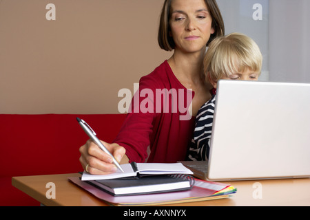 Mother taking notes while son (4-5 Years) sitting on her lap Stock Photo