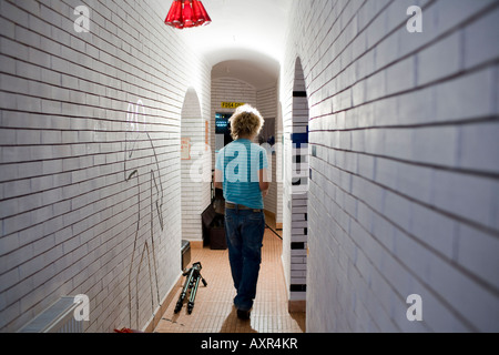 rear view of man walking through a passage made from white bricks and a figure drawn on a side of the wall moving opposite him Stock Photo