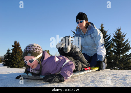 Mother preparing to give daughter a little push down a tobogganing hill Stock Photo