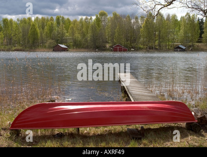 Red fiberglass rowboat / skiff / dinghy upside down at riverbank , Finland Stock Photo