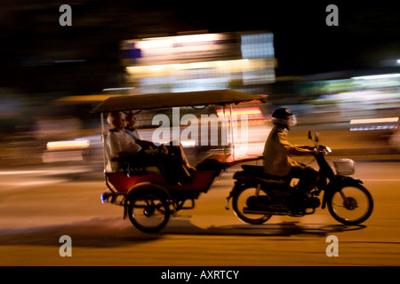 a motorcycle zooms past pulling a rickshaw in Siem Reap, Cambodia Stock Photo