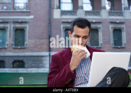 Man sitting on a bench and eating a sandwich Stock Photo