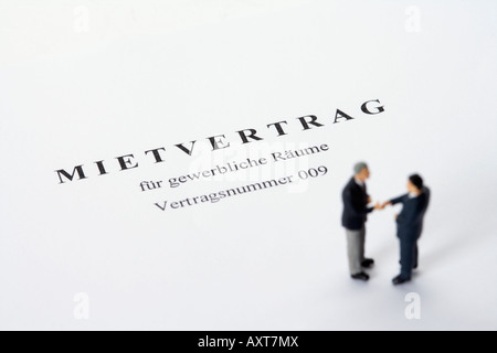 Businessmen figurines standing on a rental agreement shaking hands Stock Photo