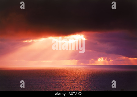 Sun rays bursting through cloudy skies over boundless ocean Stock Photo