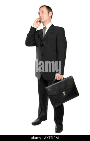 Business man standing in a black suit holding a cellphone in his hand making a phone call talking to someone some business issue. Background is white. Stock Photo