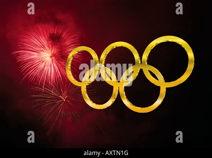 Golden olympic rings against a dark sky partially filled with deep red fireworks Stock Photo