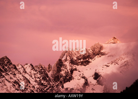 Last rays of setting sun with spectacular pink clouds closing in over snow covered peaks of Grands Montets, Chamonix-Mont Blanc Stock Photo