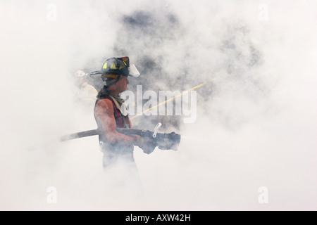 Firefighter holding a hoseline spraying the remaining fire Stock Photo