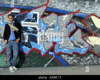 young fair-haired fashionable man stands in front of wall with colourful graffiti, USA, Bronx, New York Stock Photo