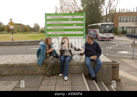 Swansea University campus, prospective student eating sandwich sitting on wall with her parents, during open day, Wales UK Stock Photo