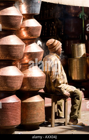 A man trades beaten copper vessels in a street in Mysore. He sits next to his wares. Stock Photo