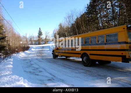 Yellow school bus travelling down a forest guarded road over ice and snow in New Brunswick Canada Stock Photo