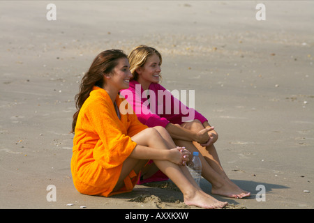 Two young women in bathrobes sitting at the beach Stock Photo