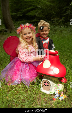 a girl dressed as a fairy and a boy dressed as a pirate play outside with a fairy toadstool toy Stock Photo