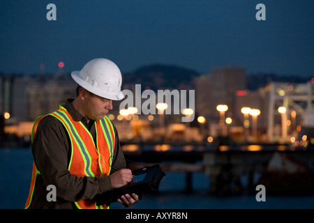 Worker wearing helmet and safety vest holding and writing on tablet pc. Room for text on right. Stock Photo