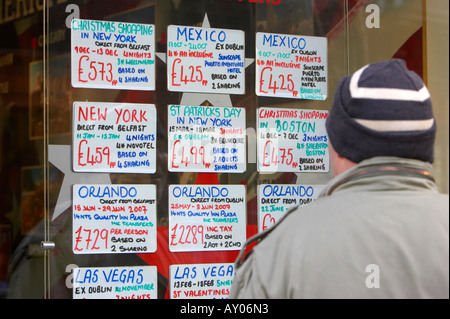 man wearing wooly cap looking at holiday offers in travel agent window on cold winter day in Belfast City Centre Stock Photo