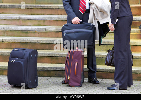 businessman and businesswoman with travel luggage standing in front of steps waiting for a taxi in Belfast City Centre Stock Photo