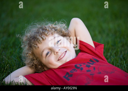 Young blonde haired boy with curly hair lying in the grass. Stock Photo