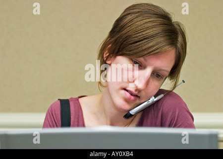 St Louis Missouri A woman talks on her cell phone while working on her laptop computer Stock Photo