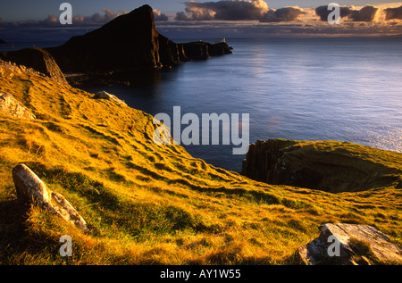 Warm glow of the setting sun cast over the curving headland at Neist Point on the Isle of Skye Scotland UK Stock Photo