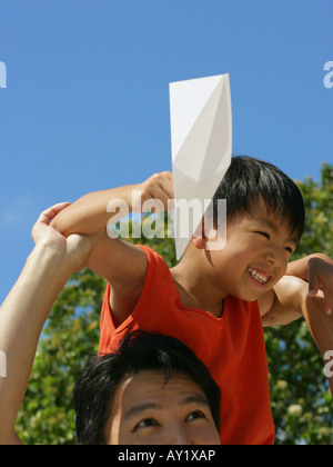 Close-up of a boy sitting on his father's shoulders holding a paper airplane Stock Photo