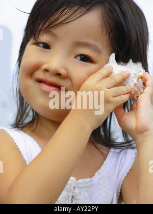 Portrait of a girl listening to a conch shell and smiling Stock Photo