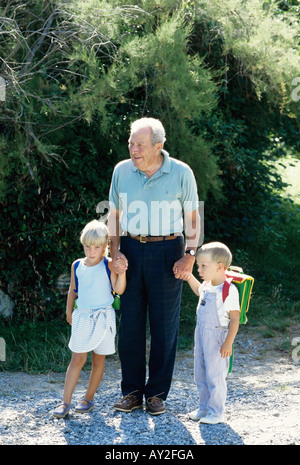 GRANDFATHER WALKING LITTLE BOY AND GIRL TO SCHOOL  FRANCE EUROPE Stock Photo