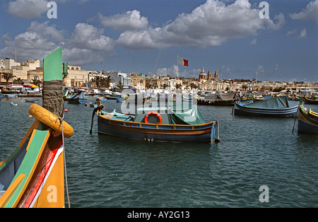 Traditional Maltese fishing boats called Luzzus moored in Marsaxlokk harbour Our Lady of Pompeii church beyond Stock Photo