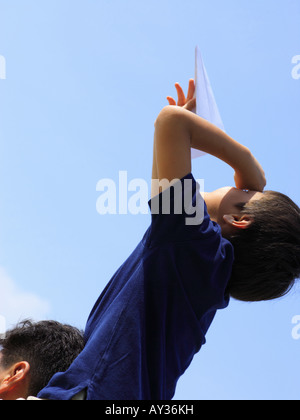 Low angle view of a boy sitting on his father's shoulders flying a paper airplane Stock Photo