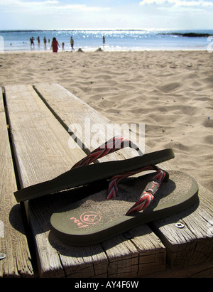 A PAIR OF FLIP FLOP SANDALS ON A WOODEN JETTY WITH A SUNNY BEACH. Stock Photo