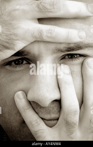Man spreading fingers across face close up black and white Stock Photo