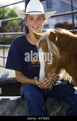 Smiling young boy wearing cowboy hat with a miniature horse Stock Photo
