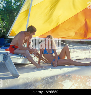 couple relaxing on beach with sailboat Stock Photo