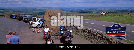 Crossing the Border from England to Scotland at Scottish Borders by road sign with few people, cars, motorbikes and distant hill Stock Photo