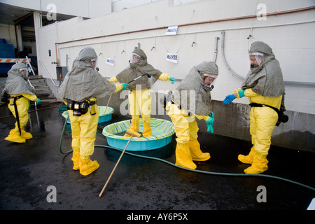 Volunteers shed chemical biological protective clothing after decontamination by colleagues with a water spray during a drill Stock Photo