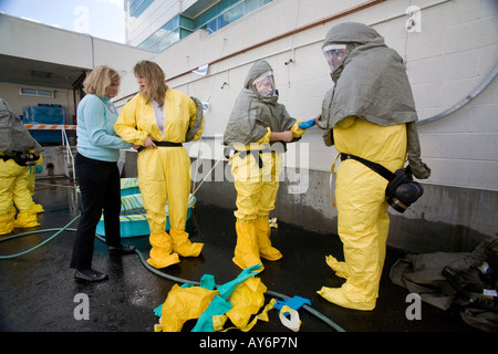 Volunteers shed chemical biological protective clothing after decontamination by colleagues with a water spray during a drill Stock Photo