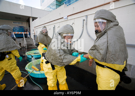 Volunteers shed chemical biological protective clothing after decontamination by colleagues with a water spray during a drill Stock Photo