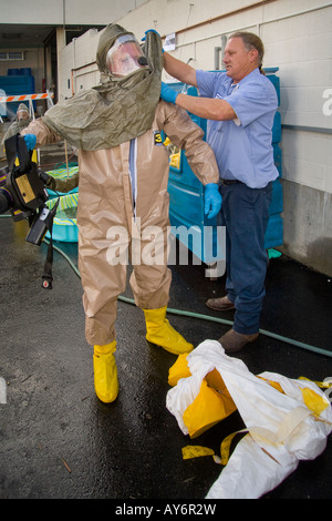 Volunteers shed chemical biological protective clothing after decontamination by colleagues with a water spray during a drill Stock Photo