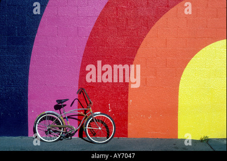 Old bike leaning against rainbow colored wall Stock Photo