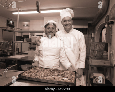 sepia toned monochrome shot of two Italian chefs posing in a professional kitchen with a big pizza Stock Photo
