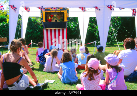 Children sitting on the ground watching a Punch and Judy show at a summer fete Suffolk England Stock Photo