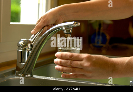 Woman filling a glass of water from the kitchen sink tap Stock Photo